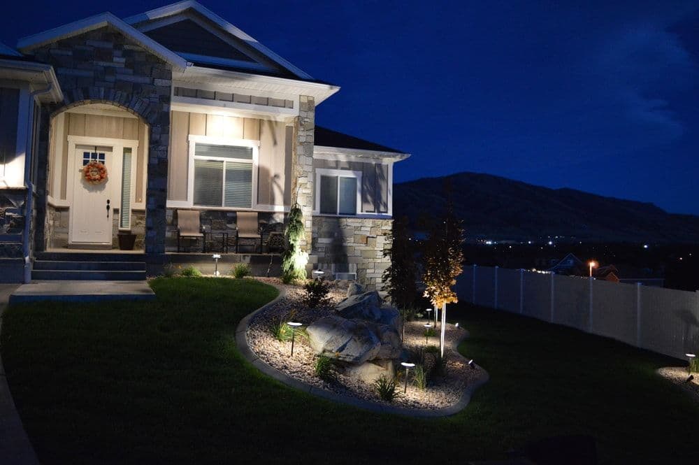 Front porch of a modern house at night, illuminated by landscape lighting and mountain backdrop.