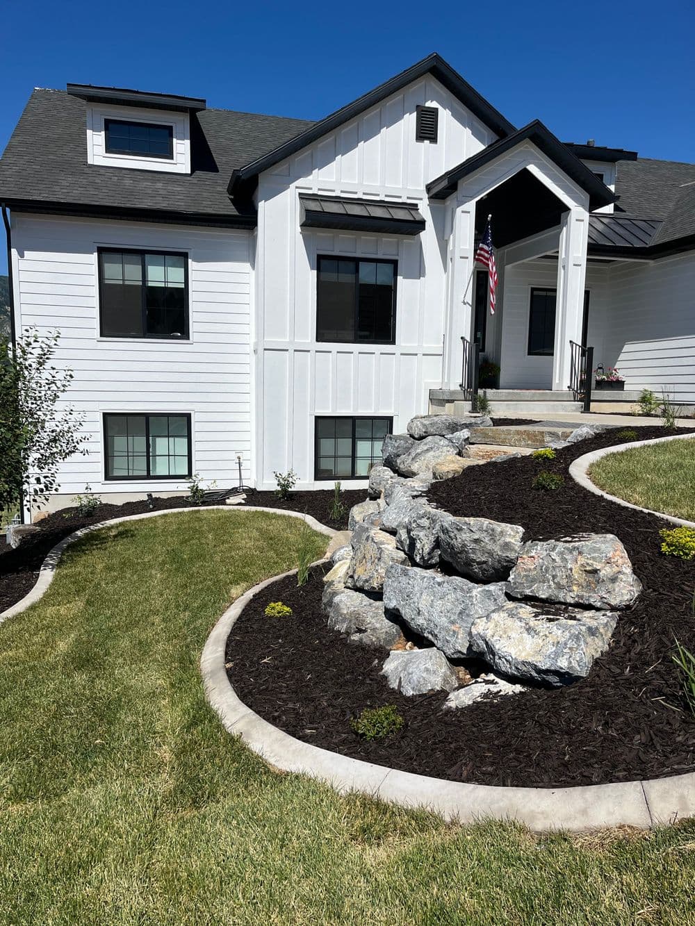 Modern white house with landscaped stone pathway and American flag in front yard.