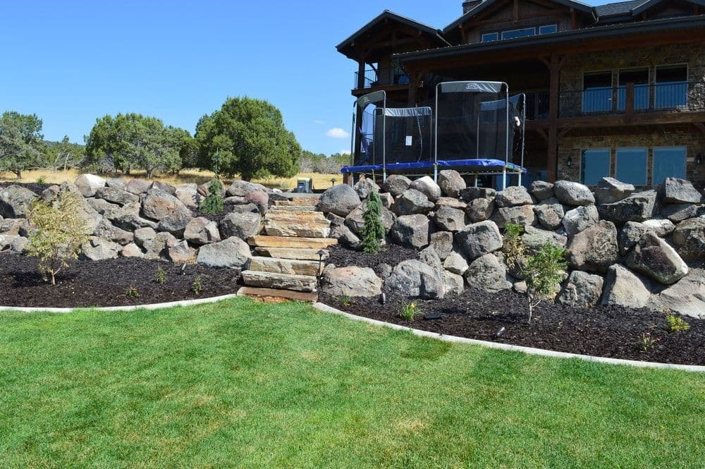 Backyard landscape featuring a stone staircase, trampoline, and manicured lawn.