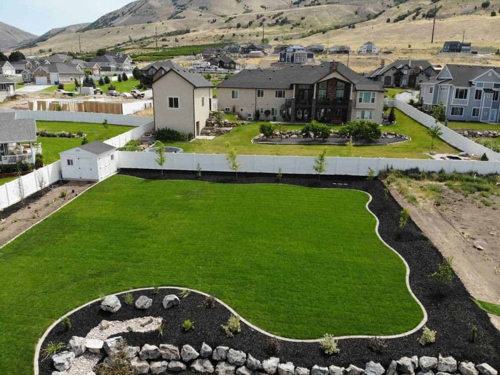 Aerial view of a landscaped backyard with green lawn, stone border, and surrounding homes.