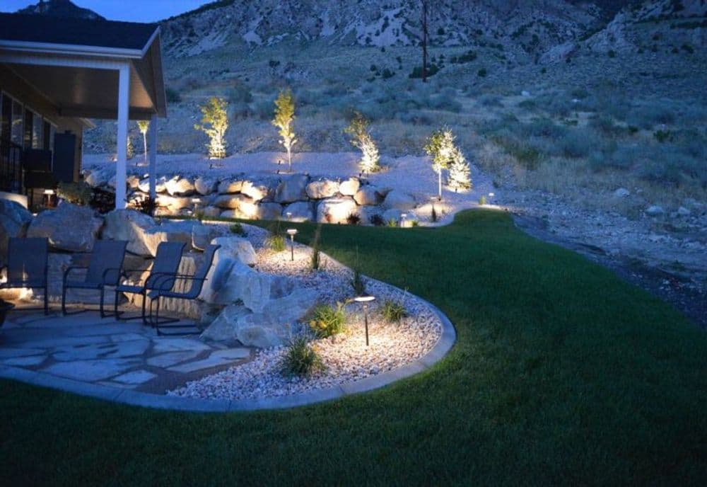 Outdoor patio with stone pathway, landscaping lights, and mountains in the background at night.